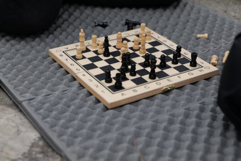 Kleines hölzernes Klappschach mit Figuren auf einer Isomatte im Freien